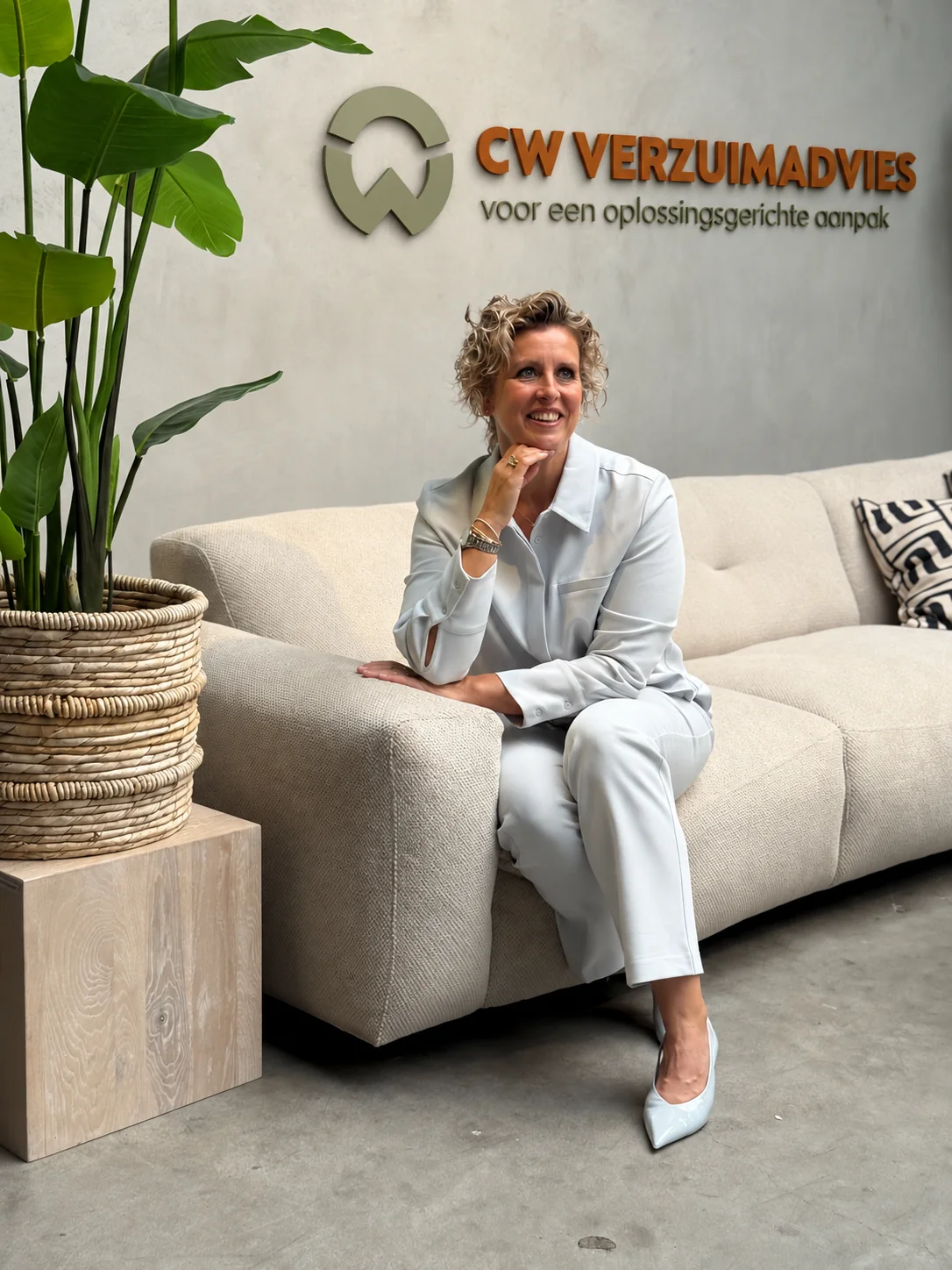 Carin op een lichte bank met het CW-logo en onderschrift op de muur